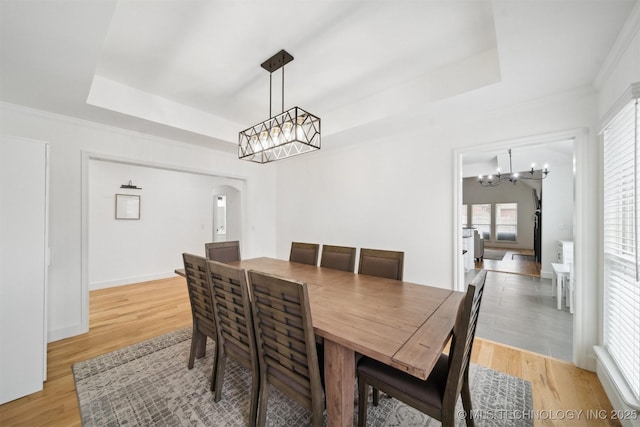 dining space featuring baseboards, an inviting chandelier, a tray ceiling, arched walkways, and light wood-type flooring