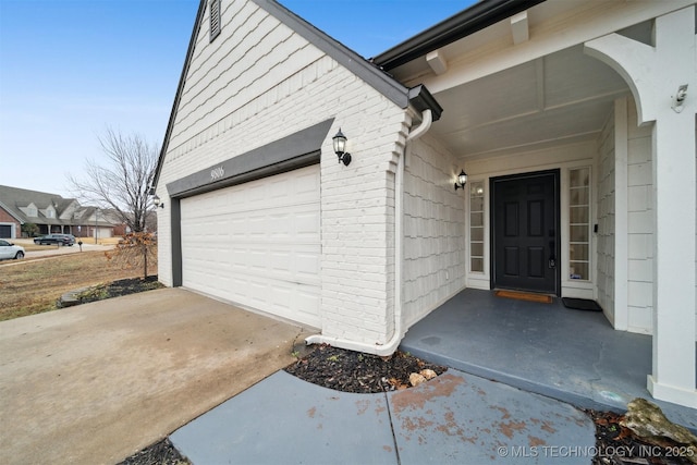 view of exterior entry featuring brick siding, an attached garage, and driveway