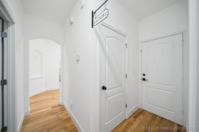 hallway with light wood-style flooring, baseboards, and arched walkways