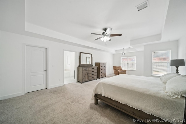 carpeted bedroom with baseboards, visible vents, ensuite bath, a tray ceiling, and ceiling fan