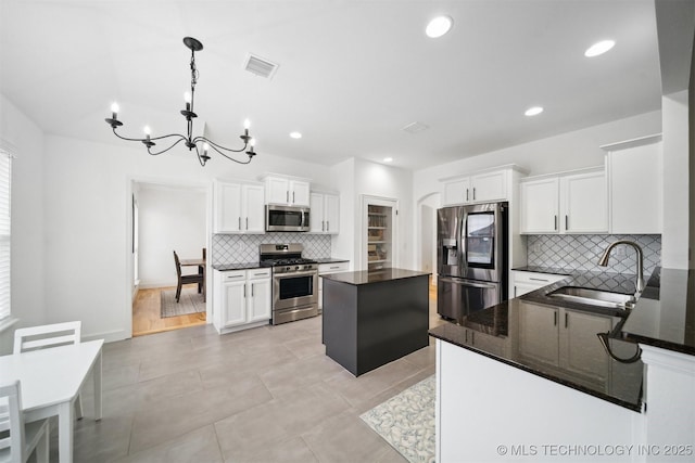 kitchen with stainless steel appliances, a sink, a chandelier, tasteful backsplash, and white cabinetry