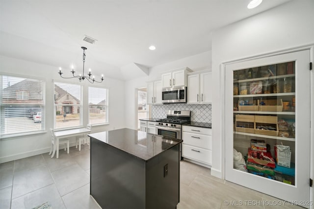 kitchen with appliances with stainless steel finishes, a chandelier, light tile patterned floors, backsplash, and a center island