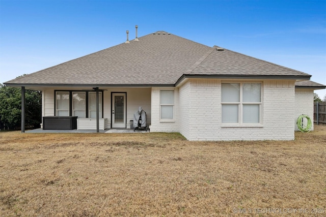 back of house featuring a lawn, brick siding, and a shingled roof