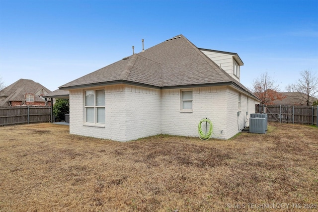 rear view of house with brick siding, central AC, a fenced backyard, and a shingled roof