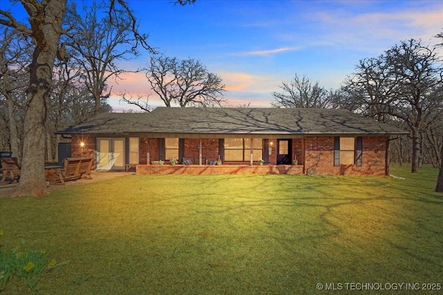 rear view of house featuring brick siding, a lawn, and roof with shingles