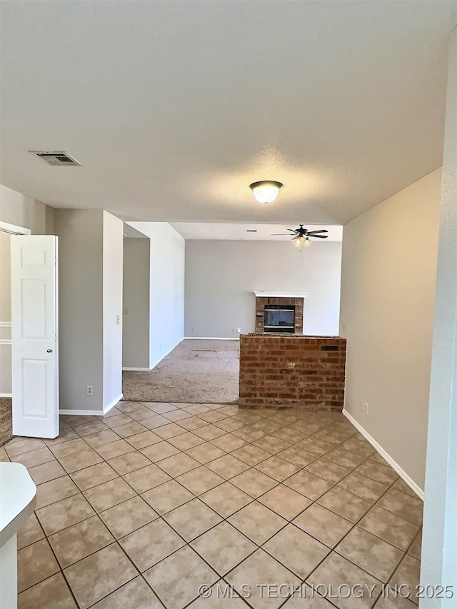 unfurnished living room featuring a glass covered fireplace, ceiling fan, baseboards, and visible vents