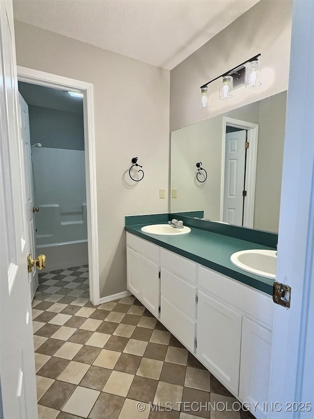 full bath with double vanity, a textured ceiling, baseboards, and a sink