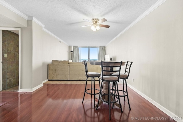 dining room featuring a ceiling fan, a textured ceiling, dark wood-style floors, crown molding, and baseboards