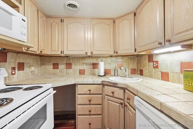 kitchen with light brown cabinets, white appliances, and a sink