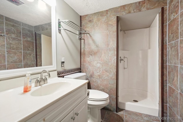 full bathroom featuring vanity, a stall shower, a textured ceiling, tile walls, and toilet