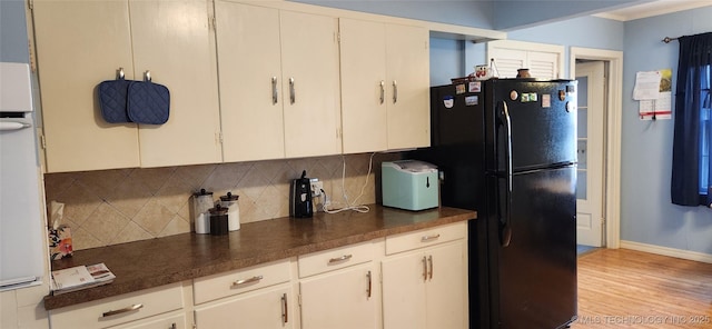 kitchen with light wood-style flooring, freestanding refrigerator, white cabinets, dark countertops, and tasteful backsplash