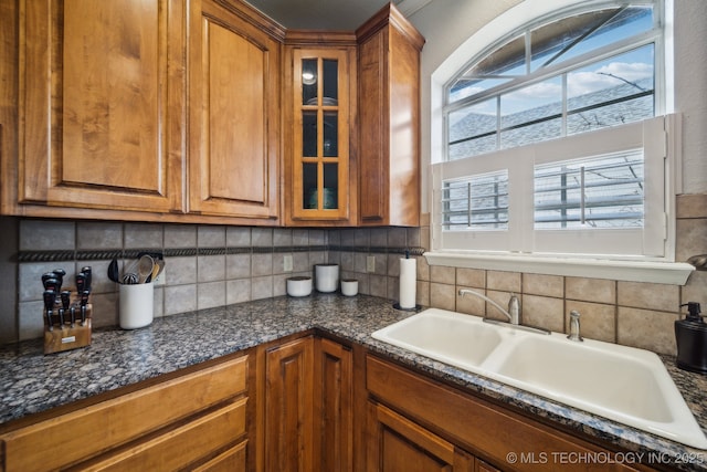 kitchen featuring plenty of natural light, glass insert cabinets, brown cabinets, and a sink