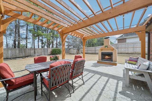 view of patio featuring a storage unit, a pergola, a fenced backyard, a lit fireplace, and outdoor dining area