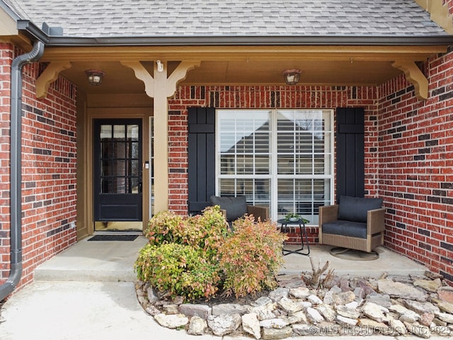 view of exterior entry featuring brick siding and roof with shingles