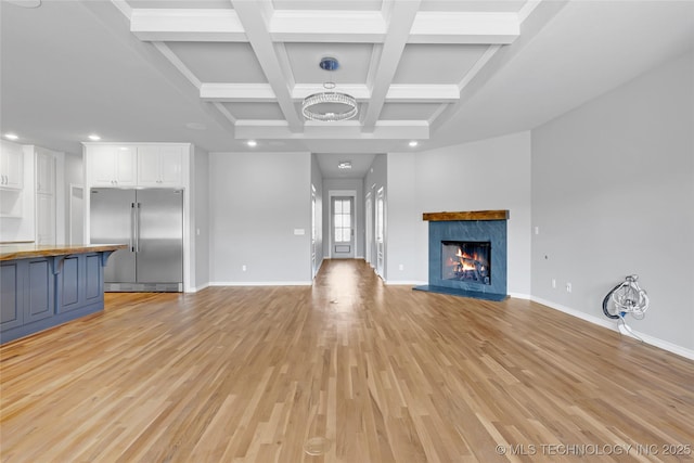 unfurnished living room featuring baseboards, beam ceiling, a fireplace, light wood-style floors, and coffered ceiling