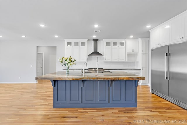 kitchen with light wood finished floors, visible vents, wall chimney range hood, recessed lighting, and built in fridge