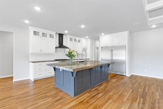 kitchen with a sink, wall chimney exhaust hood, light wood-type flooring, and stainless steel appliances