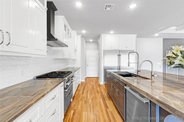 kitchen featuring visible vents, wall chimney range hood, appliances with stainless steel finishes, white cabinetry, and a sink