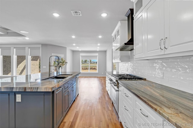 kitchen with white cabinets, wall chimney exhaust hood, light wood-style flooring, and a sink