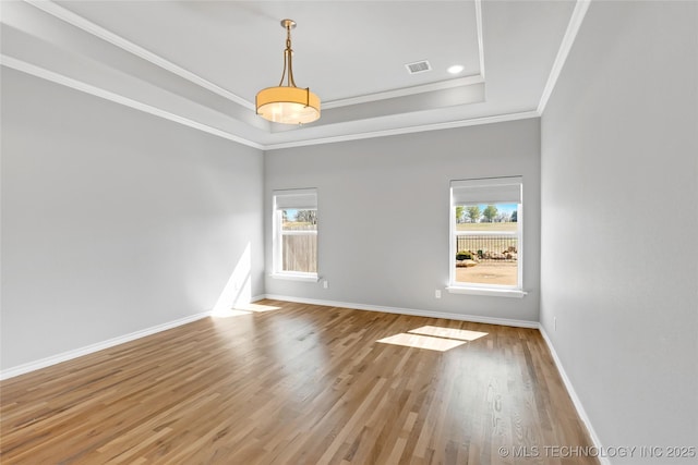 empty room with a wealth of natural light, a tray ceiling, visible vents, and wood finished floors