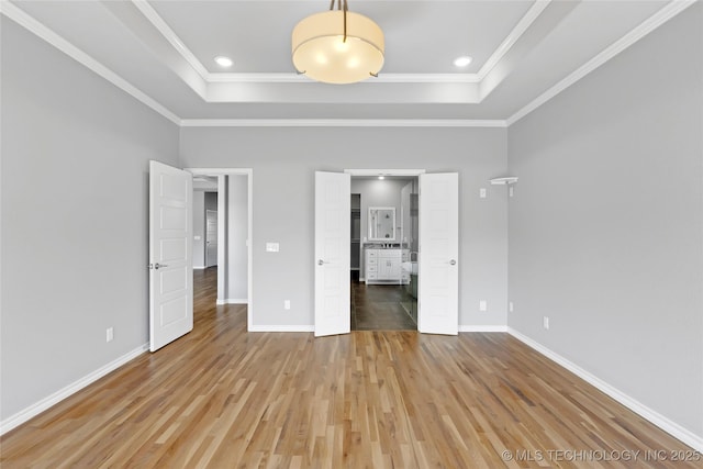 unfurnished bedroom with light wood-style flooring, baseboards, a tray ceiling, and ornamental molding