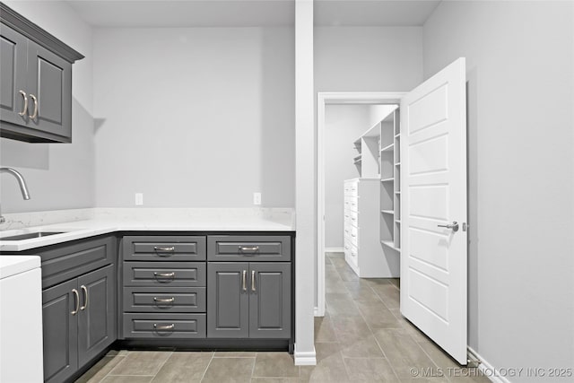 kitchen featuring gray cabinetry, light stone countertops, baseboards, and a sink