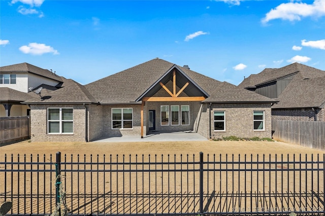 view of front of property with brick siding, a patio area, a shingled roof, and a fenced backyard