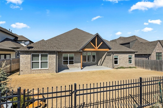 view of front of home with brick siding, a patio, a fenced backyard, and roof with shingles