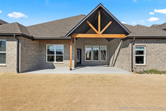 back of property featuring a yard, a patio, brick siding, and roof with shingles