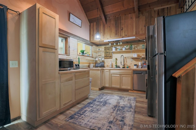 kitchen with wooden walls, light wood-style flooring, vaulted ceiling with beams, light brown cabinetry, and appliances with stainless steel finishes