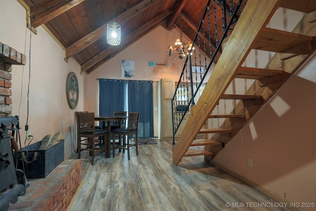 dining area with beam ceiling, wood finished floors, an inviting chandelier, wooden ceiling, and stairs