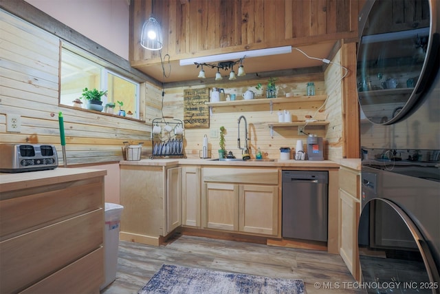 kitchen featuring wood walls, light wood-type flooring, stainless steel dishwasher, stacked washer / drying machine, and a sink