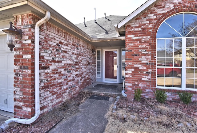 doorway to property featuring an attached garage, brick siding, and roof with shingles