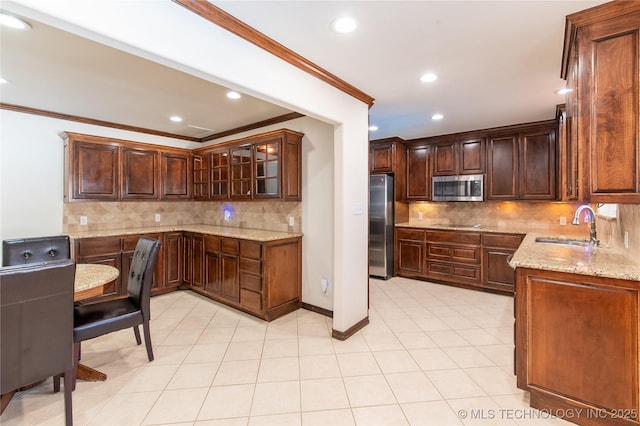 kitchen featuring glass insert cabinets, light stone countertops, ornamental molding, stainless steel appliances, and a sink