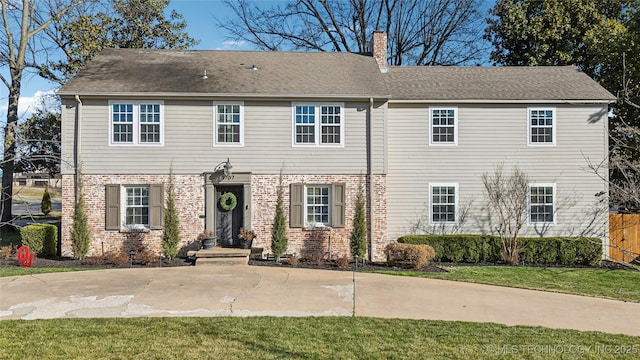 colonial-style house featuring brick siding, a chimney, a front lawn, and a shingled roof