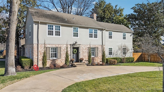 colonial house with brick siding, a shingled roof, fence, a front yard, and a chimney