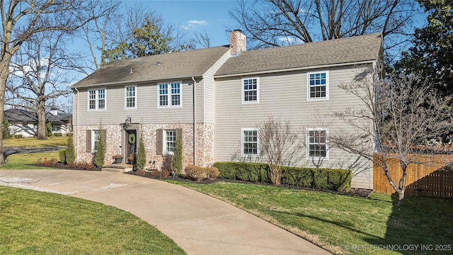 colonial home with brick siding, a front yard, roof with shingles, and a chimney