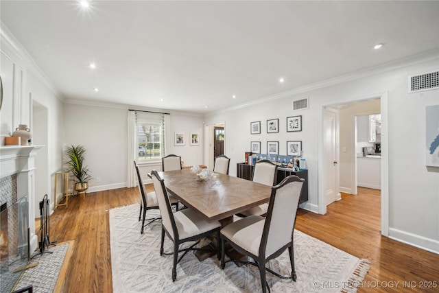 dining area featuring visible vents, crown molding, baseboards, light wood-type flooring, and a premium fireplace