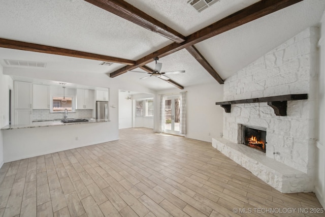 unfurnished living room with a ceiling fan, wood finished floors, visible vents, vaulted ceiling with beams, and a fireplace