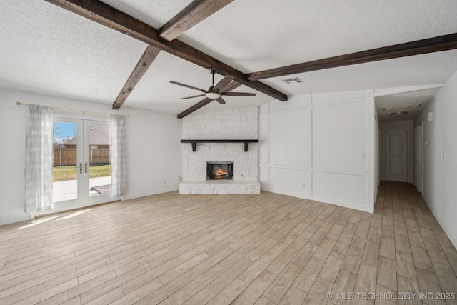 unfurnished living room featuring wood finished floors, visible vents, a stone fireplace, french doors, and a textured ceiling