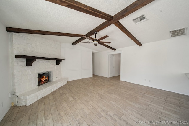 unfurnished living room featuring visible vents, a textured ceiling, a stone fireplace, and lofted ceiling with beams