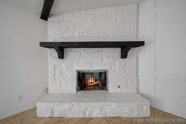 details featuring beam ceiling, a textured ceiling, wood finished floors, a fireplace, and a decorative wall