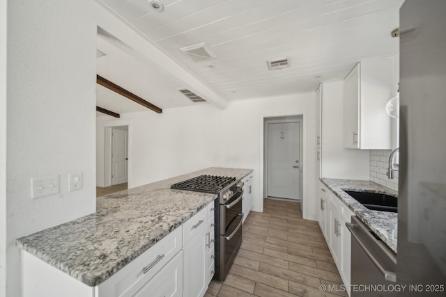 kitchen featuring visible vents, decorative backsplash, stainless steel appliances, white cabinetry, and a sink