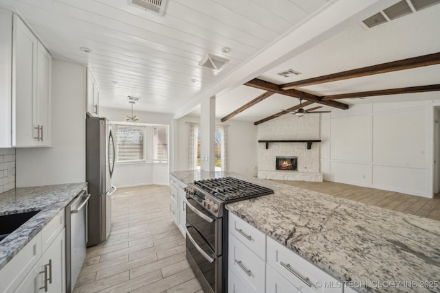 kitchen with visible vents, open floor plan, stainless steel appliances, a stone fireplace, and decorative backsplash