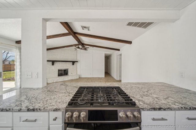 kitchen with lofted ceiling with beams, visible vents, a stone fireplace, and stainless steel gas range