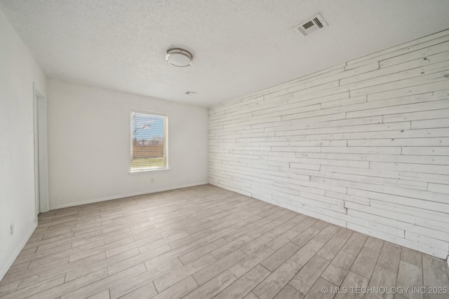 empty room with wood finished floors, visible vents, wood walls, and a textured ceiling