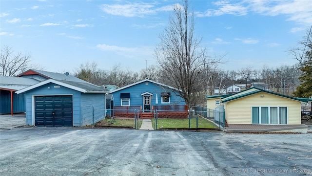 view of front facade featuring a fenced front yard, a detached garage, aphalt driveway, and an outbuilding