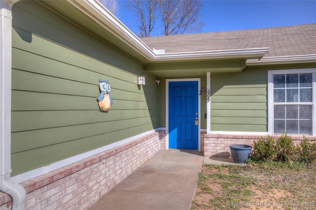 doorway to property featuring brick siding and roof with shingles