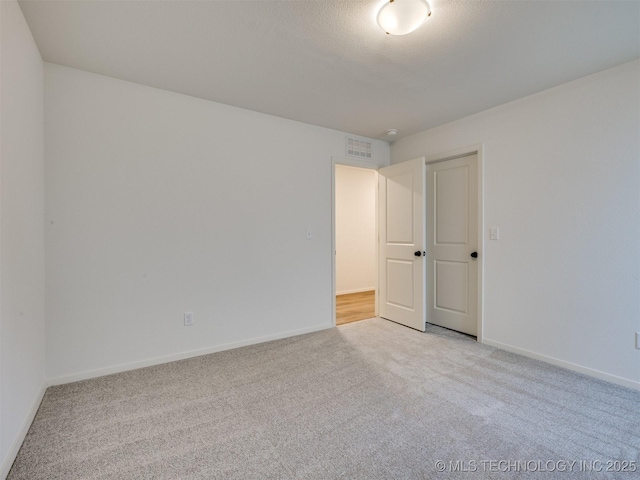 empty room featuring visible vents, light carpet, and baseboards