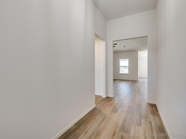 hall with light wood finished floors, visible vents, and baseboards